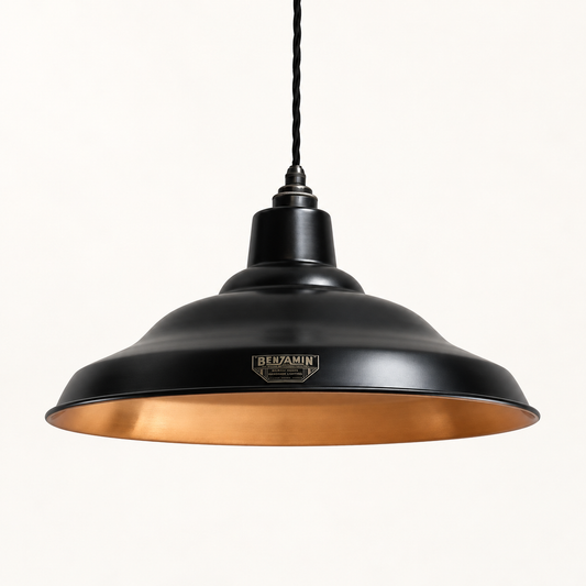 A black metal pendant light with a warm copper interior and a visible Benjamin brand badge on the front, suspended against a plain off-white background.