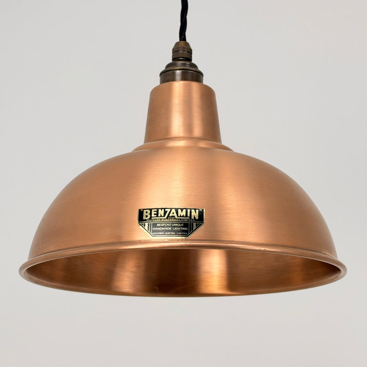 A copper-colored metal dome pendant light from Benjamin, suspended against a plain light gray background.