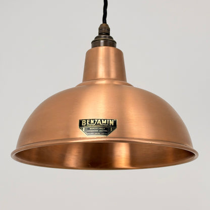 A copper-colored metal dome pendant light from Benjamin, suspended against a plain light gray background.