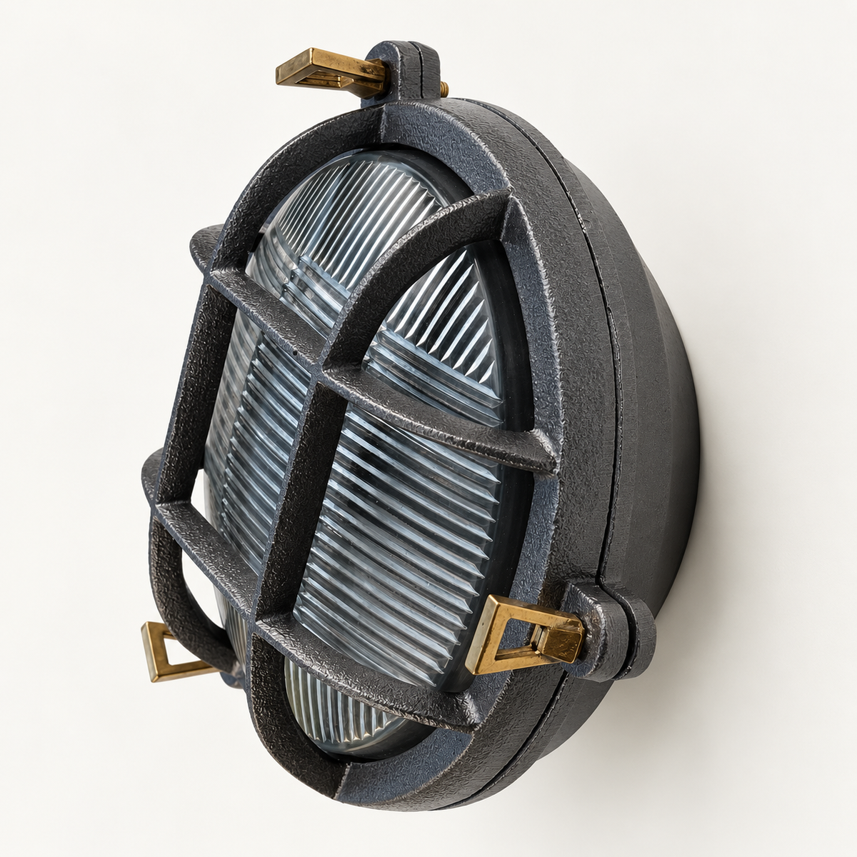 A vintage-style industrial wall light fixture with a textured dark grey cast body, a ribbed clear glass lens, and brass-toned metal mounting brackets, shown against a plain off-white background.