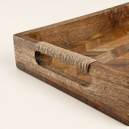 A close-up of a wooden serving tray with a geometric parquetry pattern and a natural fiber-wrapped handle, set against a plain off-white background.