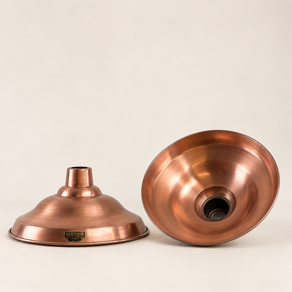 Two copper-colored metal lamp shades shown on a plain light beige studio background, one upright and one tipped on its side to show the interior.