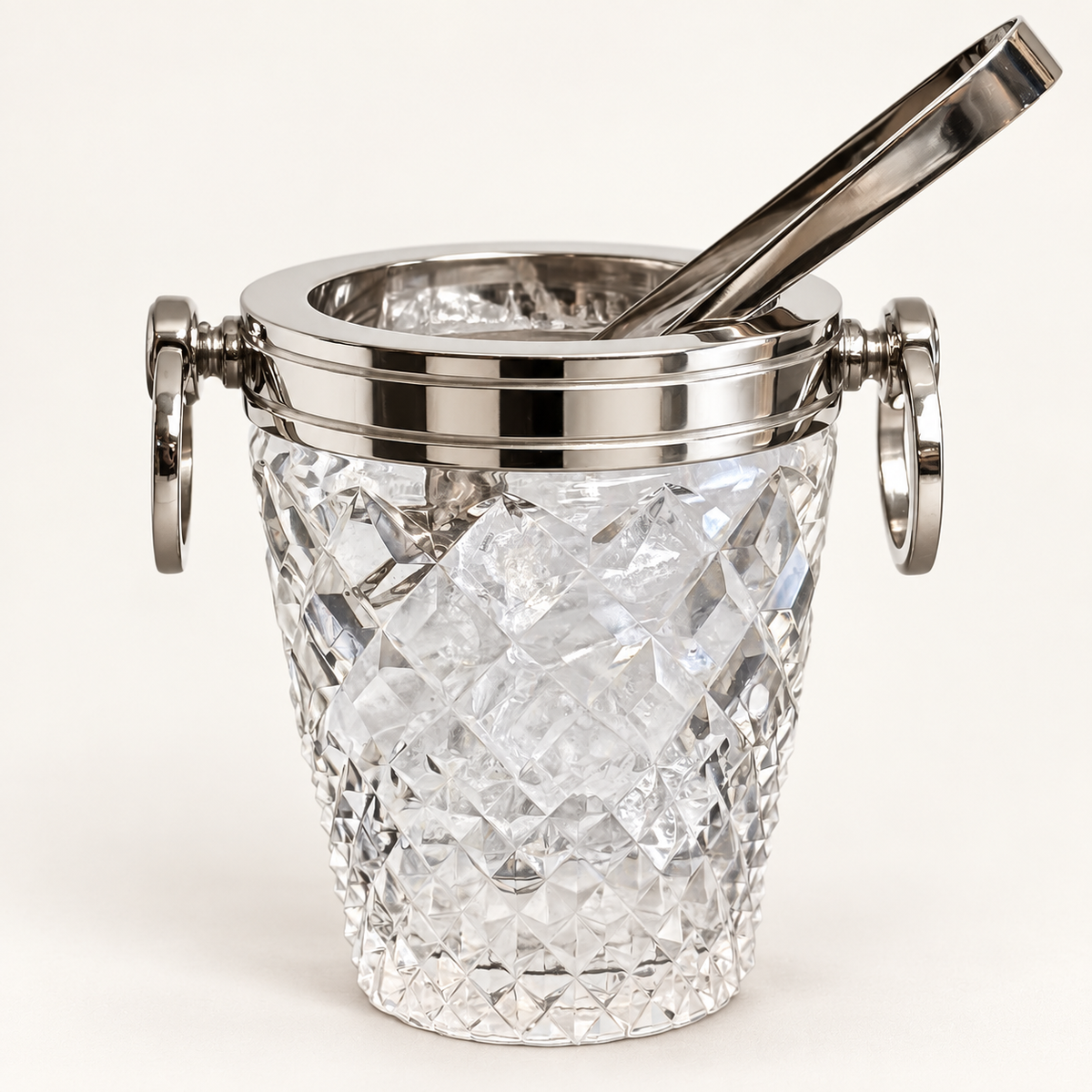 A clear cut-crystal ice bucket with a polished silver-tone metal rim, side handles, and a matching metal tong resting inside, shown on a clean white background.