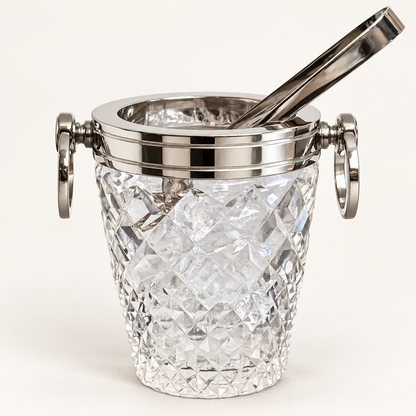A clear cut-crystal ice bucket with a polished silver-tone metal rim, side handles, and a matching metal tong resting inside, shown on a clean white background.