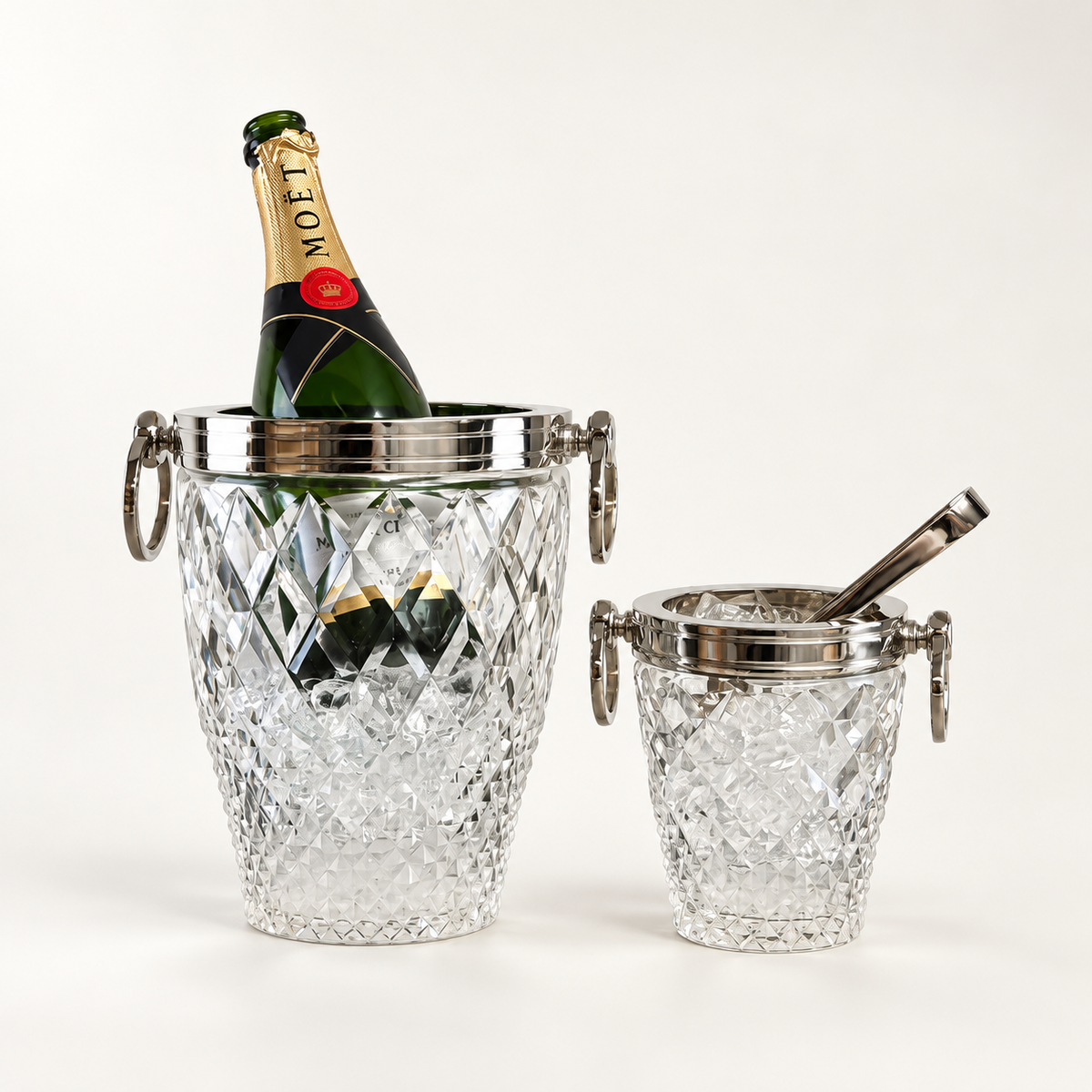 Two clear cut-crystal champagne buckets with silver-tone metal handles and lids, one larger bucket holding a Moët bottle and ice, and one smaller bucket with a spoon, photographed on a clean white background.