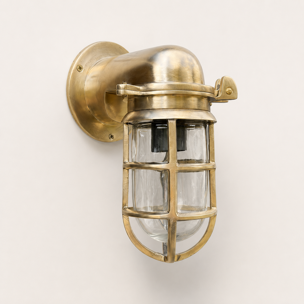 Industrial-style wall sconce with a brass-finished metal mounting bracket, protective cage guard, and clear glass panels, shown against a plain off-white background.