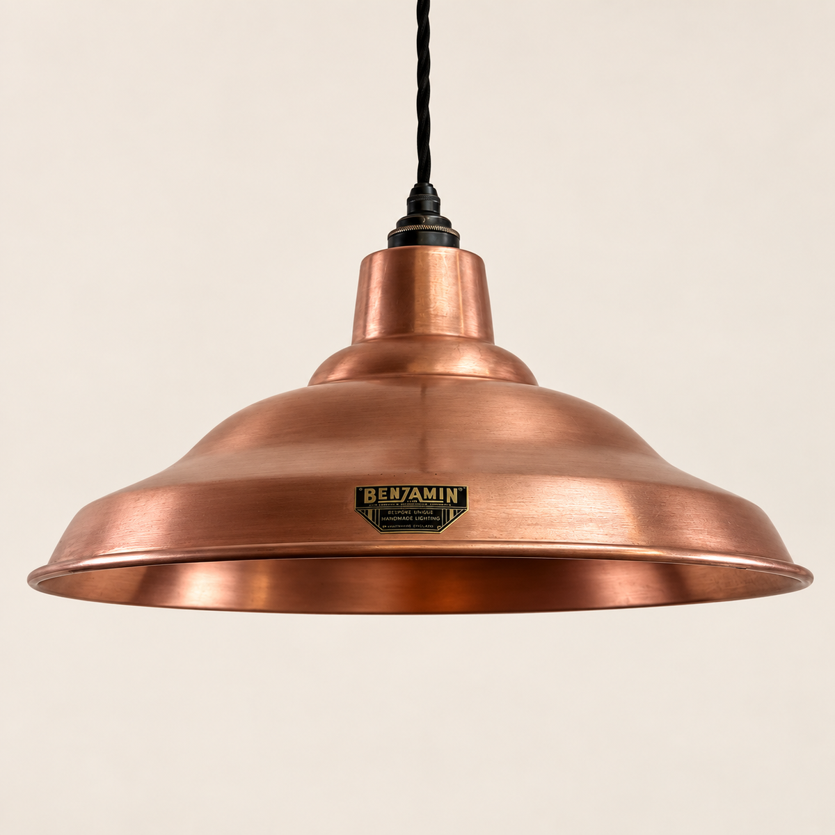 A copper-colored pendant light shade with a black hanging cord and a small black and gold 'BENJAMIN' brand plaque on the front, set against a solid off-white background.