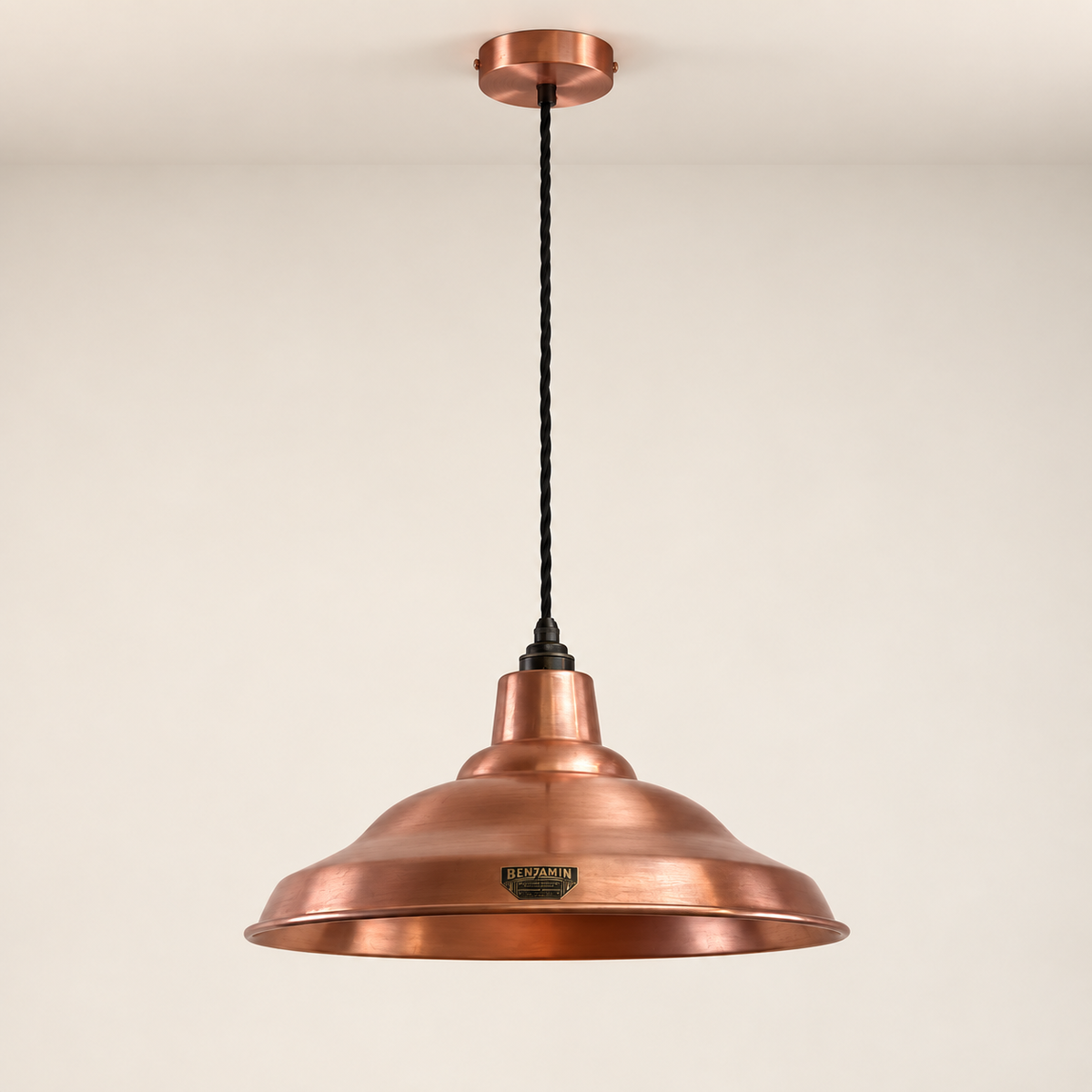 A copper pendant light with a wide, shallow dome shade, a black twisted cord, and a round ceiling canopy, shown against a plain off-white wall.