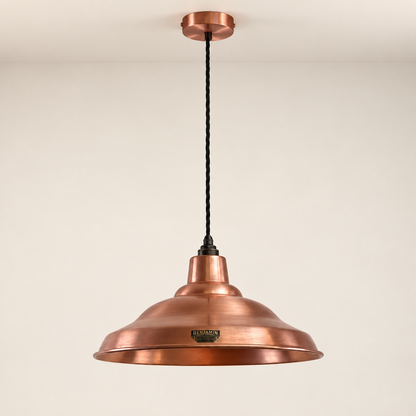 A copper pendant light with a wide, shallow dome shade, a black twisted cord, and a round ceiling canopy, shown against a plain off-white wall.