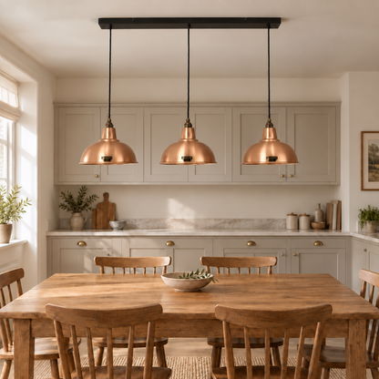 Three copper dome pendant lights hanging from a black ceiling bar over a wooden dining table in a bright, modern kitchen.