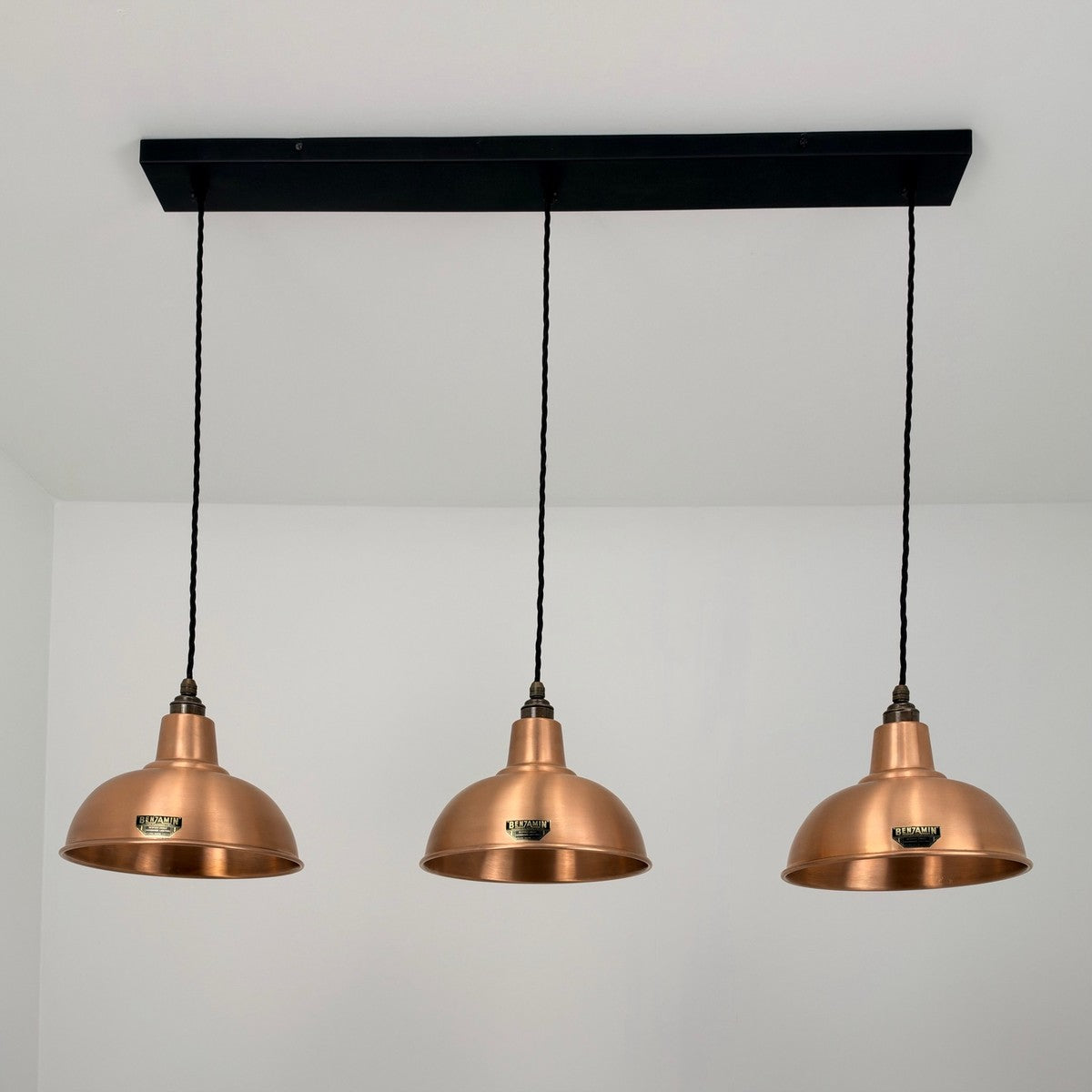Three copper dome pendant lights hanging from a black rectangular ceiling canopy against a white wall.