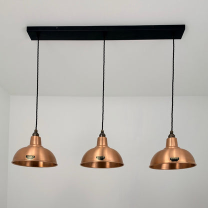 Three copper dome pendant lights hanging from a black rectangular ceiling canopy against a white wall.