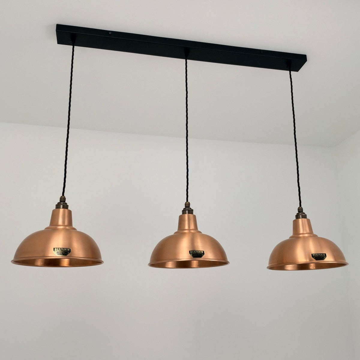 Three copper dome pendant lights hanging from a black rectangular ceiling bar against a white wall.