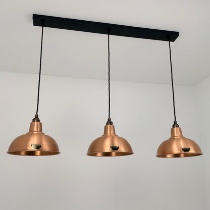 Three copper dome pendant lights hanging from a black rectangular ceiling bar against a white wall.