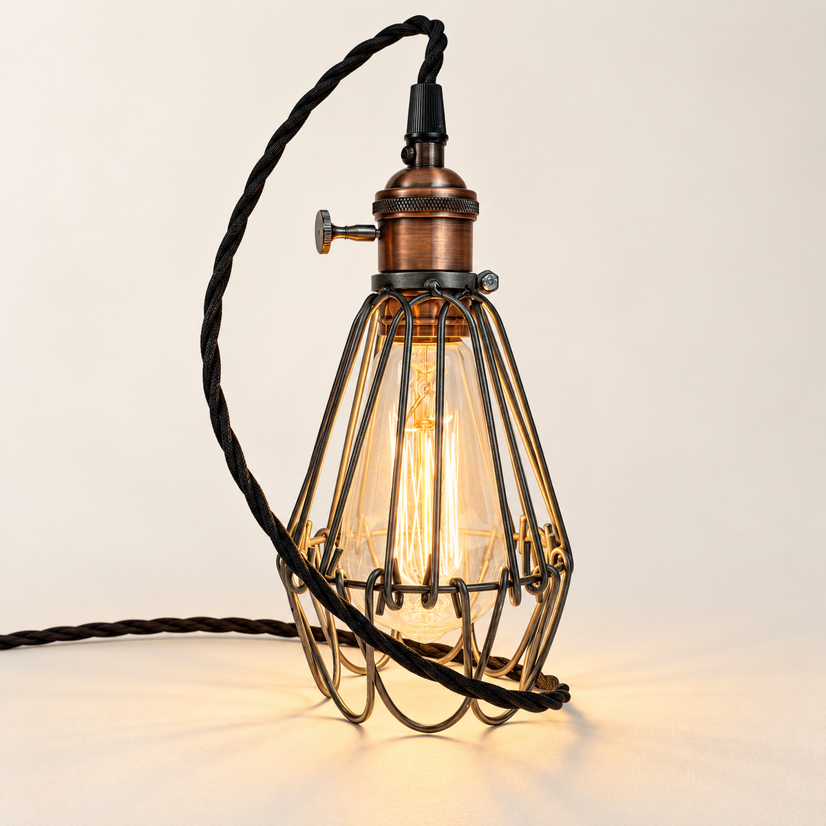 Hemsby raw steel cage lamp with copper finish holder and black fabric cable, illuminated in the studio