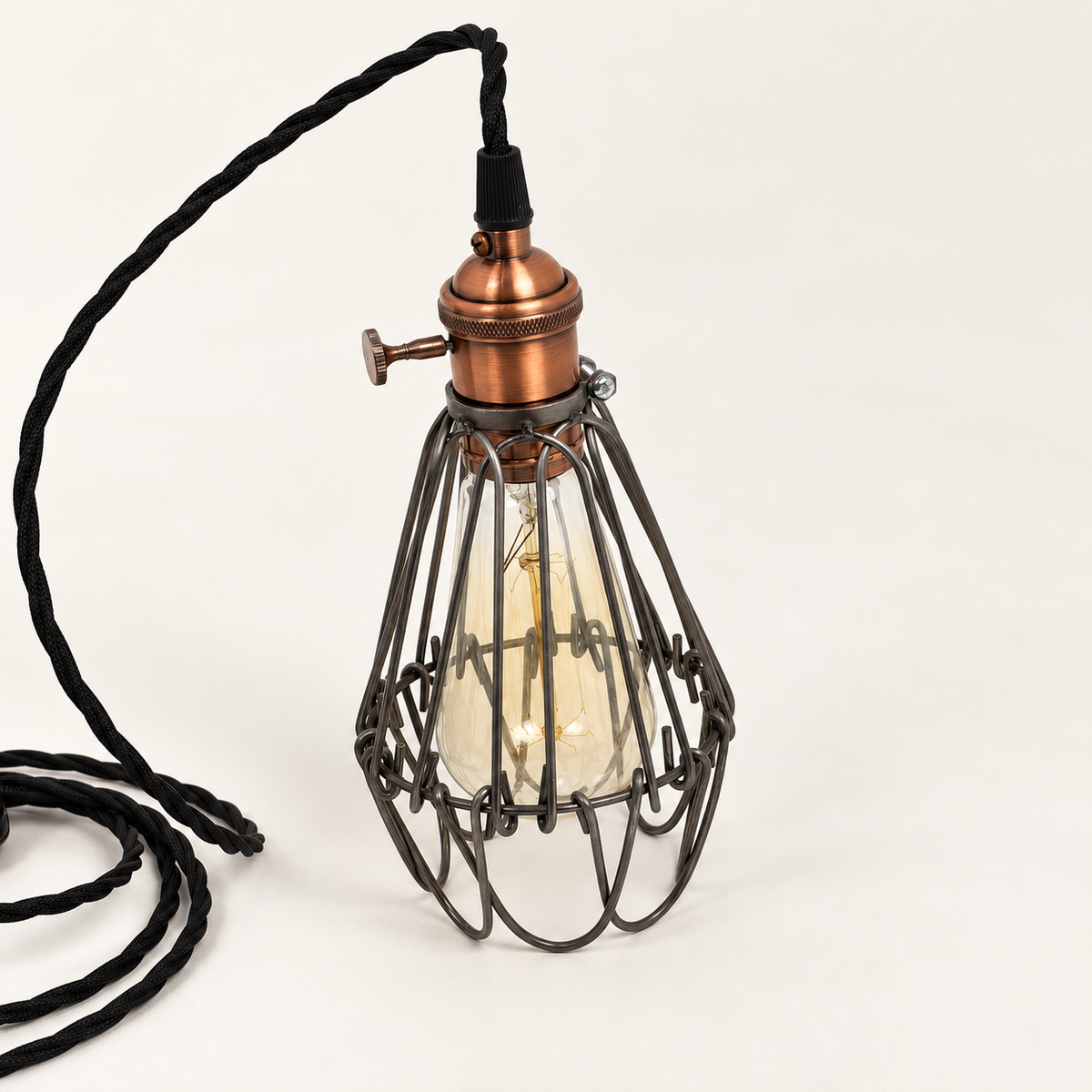 Three-quarter studio view of the Hemsby raw steel cage lamp showing the copper finish holder and rotary switch