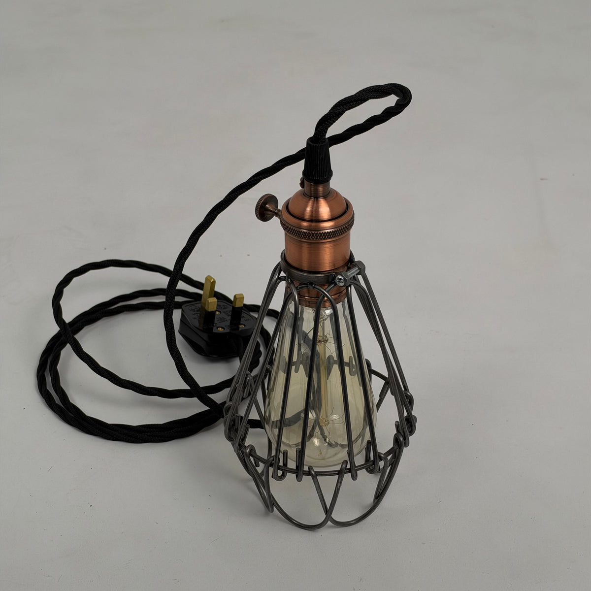 Original photograph of the Hemsby raw steel cage lamp with copper finish holder, black fabric cable and UK three-pin plug