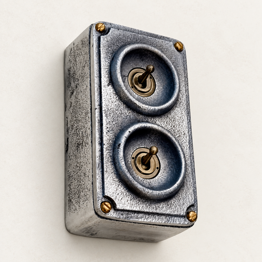 2-gang raw metal toggle light switch with brass details, angled studio view.